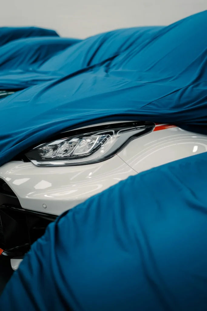 A blue cloth being drawn back from a white car