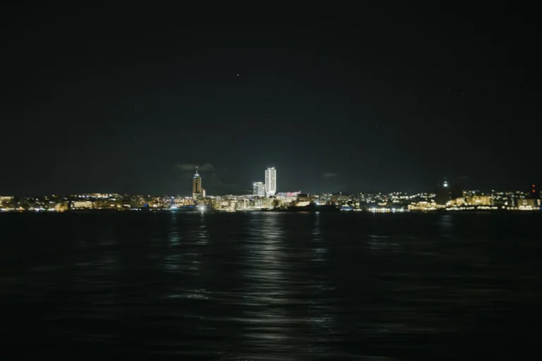 The illuminated coastline from the water · AFLOAT — Exclusive Networking at Sea